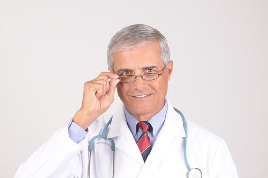 Portrait of a Middle Aged  Male Doctor in Lab Coat with Stethoscope adjusting his eye glasses - gray background
