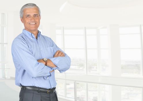 A smiling casually dressed mature businessman standing in front of a large modern office window. High key office background with copy space., copy space Horizontal format.