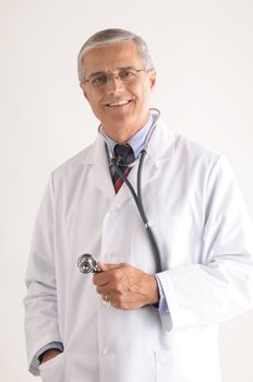 Middle aged doctor holding stethoscope over light gray background vertical composition torso only