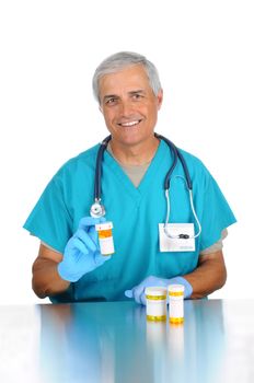 Smiling middle aged doctor holding up a prescription bottle filled with medication with two additional bottles on the table in front of him. Vertical format isolated on white.