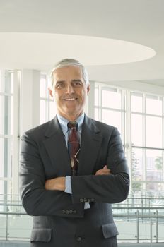 Smiling Middle Aged Businessman with his arms crossed in modern office setting