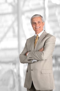 A mature businessman with his arms folded against blurred modern office interior. Vertical Format.