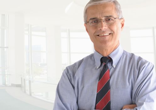 Business man portrait in high key office setting. Middle aged man is smiling at the camera and has his arms folded. Closeup head and shoulders only.