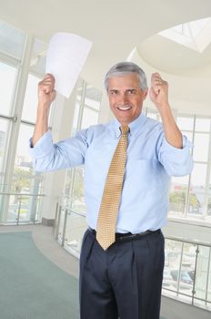 Happy Middle Aged Businessman In Office Holding a Contract in his Hands that are Raised in a victory gesture vertical format