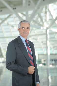 Middle aged businessman standing in modern office lobby. Vertical format with man smiling at the camera.