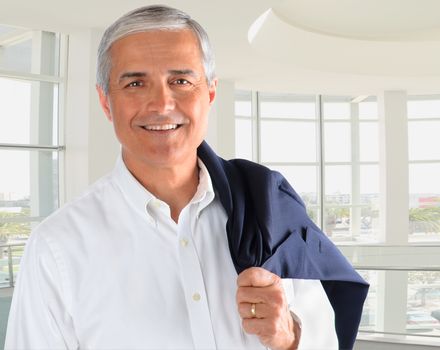 Portrait of a casually dressed businessman in a modern office building. Man is smiling holding his jacket over his shoulder.