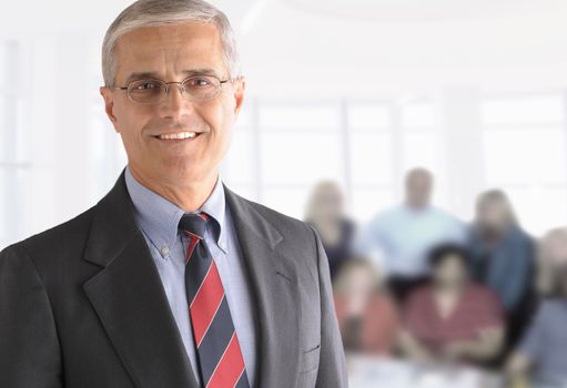 Friendly senior businessman in a modern office. With out-of-focus business team seated behind.