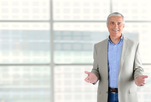 Closeup of a smiling middle aged businessman gesturing with both hand. Man is standing in front of a large modern office building window. Horizontal Format.