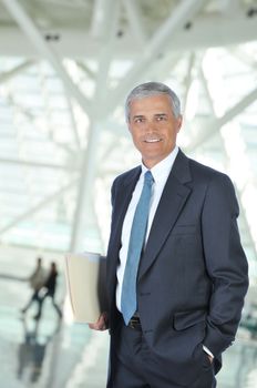 Middle aged Businessman in Lobby of Modern Building carrying file folder with out of focus people in background