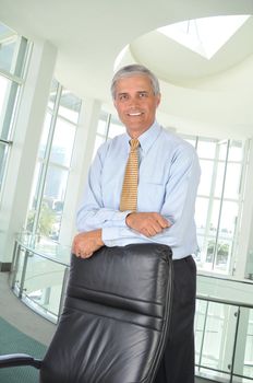 Middle aged Businessman Standing and Leaning on Back of His Chair in office setting