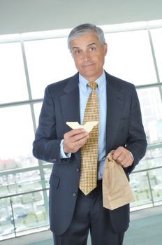 Middle aged Businessman in office building holding brown bag and sandwich