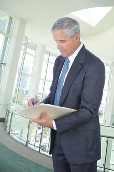 Standing Middle aged Businessman Writing in File Folder in Office Setting