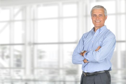 A smiling casually dressed mature businessman standing in front of a large modern office window. The man is set ot the right of the frame leaving room for your copy. Horizontal format.