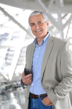 A Casual Businessman with a Cell Phone standing in a modern office building. The man is wearing jeans and a sports coat, a hand in one pocket and phone in the other.