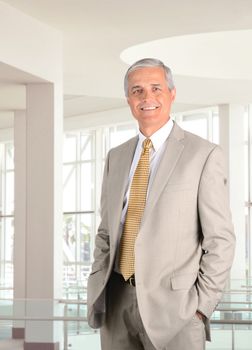 Closeup of a middle aged businessman standing in a modern office setting with his hands in pants pockets. Vertical format.