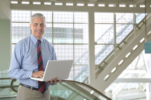 Middle aged Businessman with White laptop computer in front of Escalator in modern office building