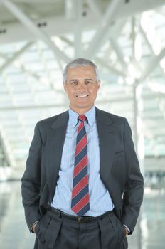Middle aged businessman standing in modern office lobby with his hands in pockets. Vertical format with man smiling at the camera.