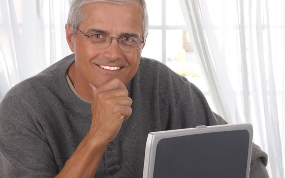 Middle aged man in front of living room window with his laptop computer.