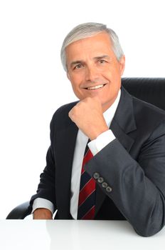 Portrait of a successful mature businessman seated at a desk with his hand on his chin. Man is smiling. Vertical format over white background.
