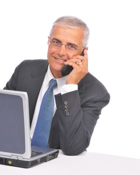 Mature Businessman seated at desk with laptop talking on cell phone isolated on white