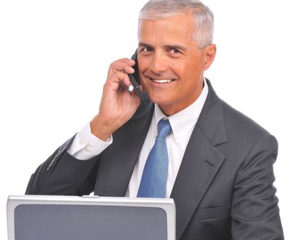 Mature Businessman seated at desk with laptop talking on cell phone isolated on white