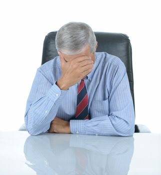 Middle aged businessman seated at his desk with his head in his hand. Square format isolated on white with reflection in desk top.