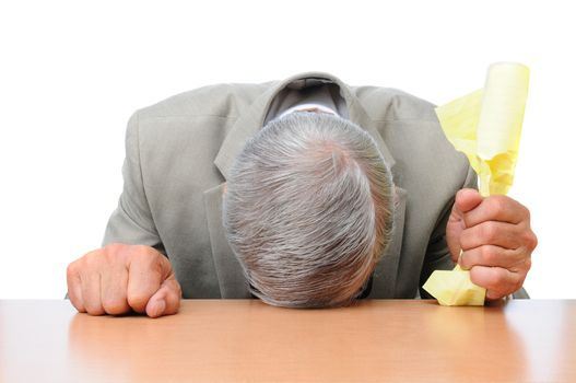 A frustrated businessman with his head on his desk and a piece of crumpled paper in one hand. Horizontal format over white.