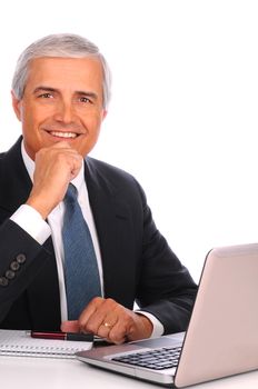 Middle aged businessman seated at his desk in front of laptop computer. Man is smiling with one hand at his chin. Vertical format over white a background.