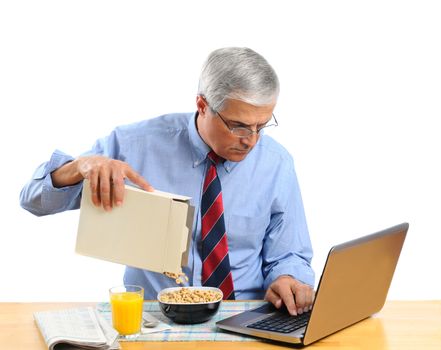 Middle aged man pouring his breakfast cereal into bowl. He is is busy working on his laptop computer and not paying attention to what he is doing. Horizontal format isolated over white.