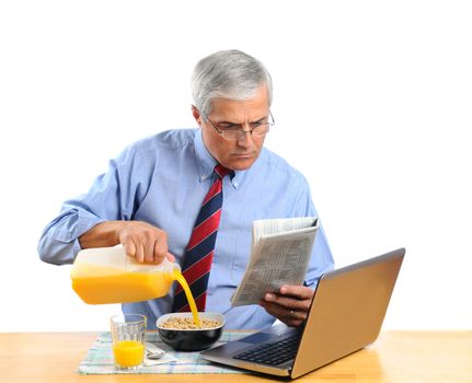 Middle aged man pouring Orange Juice into his breakfast cereal bowl instead of milk . He is in front of his laptop computer reading the morning newspaper. Horizontal format isolated over white.