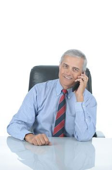 Smiling Middle aged businessman sitting at his desk talking on his cell phone isolated over white with reflection in desk top