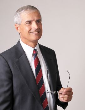 Profile Portrait of a Smiling Middle Aged  Businessman holding his glasses against a gray background