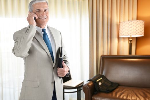 A mature businessman talking on his cell phone in a hotel room. Business travel concept.