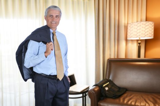 A mature businessman in a hotel room with this jacket over his shoulder. Business travel concept.