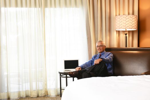 Mature Businessman sitting on the couch in his hotel room with his leg crossed. Business travel concept.