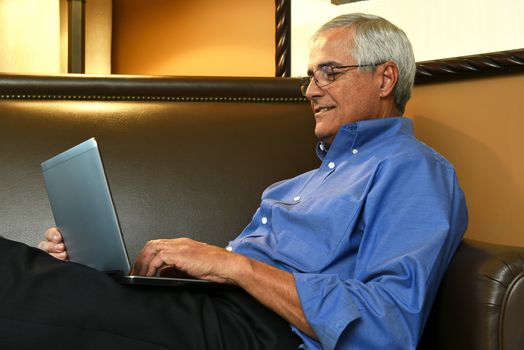 Closeup of a senior businessman sitting on a sofa in his hotel room while using a tablet computer. The man is seen from the side.