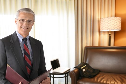 Portrait of a mature businessman in a hotel room holding a folder. Business travel concept.