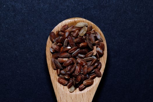 Black wild rice on a wooden spoon on black background. Negative space and copy space. Concept of healthy food.