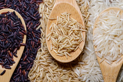 Black wild rice, brown wild rice and white jasmine rice in wooden spoon flat lay. Creative layout. Food concept