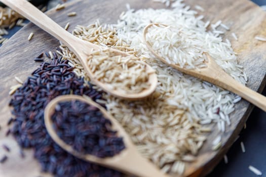 Black wild rice, brown wild rice and white jasmine rice in wooden spoon flat lay. Creative layout. Food concept. Focus on brown rice.