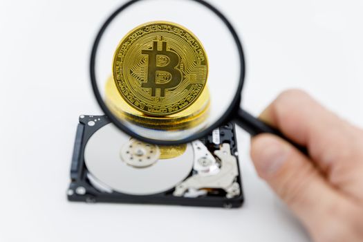 Magnifying glass over a gold bitcoin token on top of an open hard drive.Worldwide virtual internet cryptocurrency and digital payment system.Digital coin money crypto currency