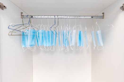 Disposable surgical masks hanging on hangers in a wardrobe closet. Concept of new normal. Concept of waring a mask becoming e new habit. Concept of adaptation during crisis and pandemic due to Covid.