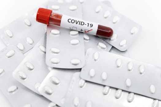Positive COVID-19 blood test tube on top of medicine. Concept of coronavirus treatment medicine.