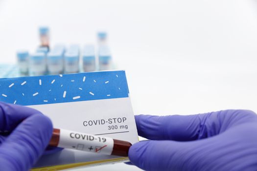 Doctor showing box of medicine with positive covid-19 test.Concept of covid stop medicine with blood tests tubes on the background.Cure for coronavirus,COVID-19 treatment.
