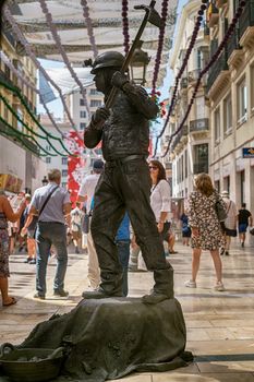 Malaga, Spain - August 03, 2018. Human statue of a miner performs on the Marques de Larios pedestrian, in the historic center of Malaga, Spain