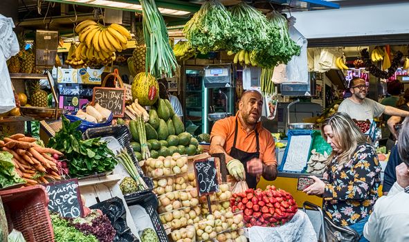 Malaga, Spain - May 05, 2018. A man sells dried fruits and vegetable stall at Ataranzanas Central Market, Malaga, Spain