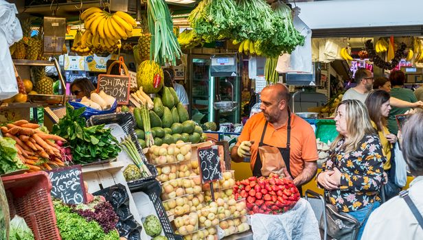 Malaga, Spain - May 05, 2018. A man sells dried fruits and vegetable stall at Ataranzanas Central Market, Malaga, Spain