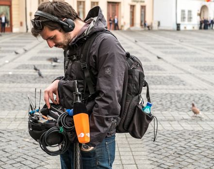 Sibiu City, Romania - 9 May 2019. lateral view of a television technician sound recording outdoor on the street maintaining a ladder