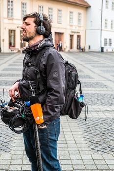 Sibiu City, Romania - 9 May 2019. lateral view of a television technician sound recording outdoor on the street maintaining a ladder