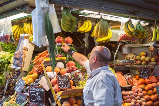 Malaga, Spain - August 28, 2018. Seller at the fresh fruit stand at the market of Ataranzanas Central Market, Malaga, Spain